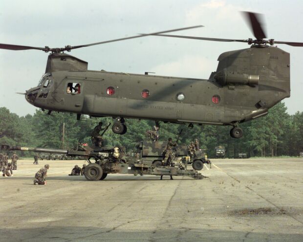 Image: Soldiers sling load a Howitzer below a CH-47 Chinook.