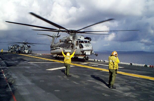 Image: A Navy Landing Signal Enlisted signals a CH-53 Super Stallion helicopter to lift off.